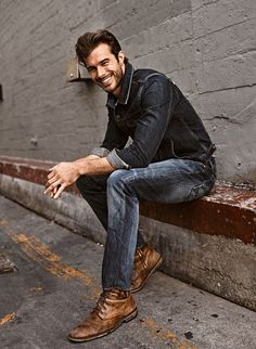 a man sitting on the side of a building while talking on a cell phone and smiling