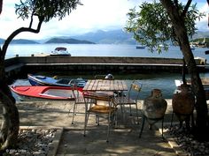 there is a table and chairs next to the water with boats in the back ground