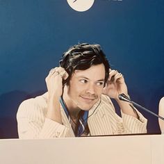 a man sitting in front of a microphone with his hand on his head and wearing a suit