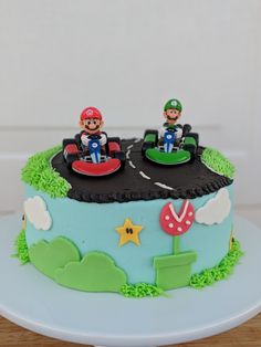 a birthday cake decorated with mario kart driving on the road and two people sitting on top