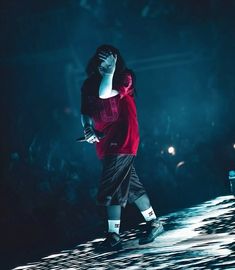 a man in red shirt and black shorts standing on stage with his hand up to his face