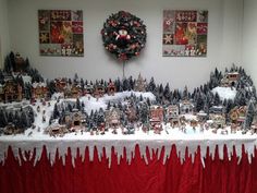 a christmas village is displayed on a table with red drapes and snow covered trees