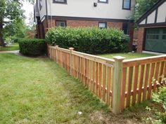 a wooden fence in front of a brick house with green grass and bushes around it