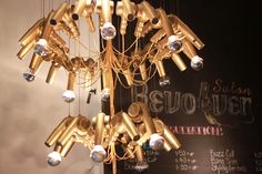 a chandelier made out of gold pipes hanging from it's ceiling in front of a chalkboard with writing on it