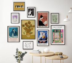 there are many framed pictures on the wall above a table with a plant in it