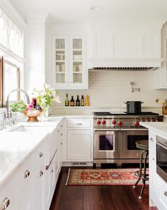 a kitchen with white cabinets and stainless steel stove top oven, hardwood flooring and an area rug