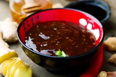 a red bowl filled with chili sauce next to sliced ginger and garlic on a table