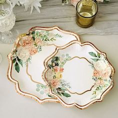 there are two plates with flowers on them next to some glasses and candlesticks