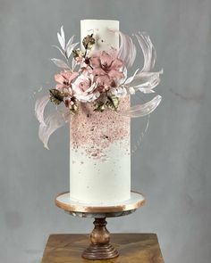 a white and pink wedding cake with flowers on top is sitting on a wooden stand