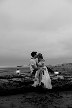 a man and woman are sitting on a log at the beach with their arms around each other