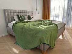 a bed covered in a green blanket sitting on top of a hard wood floor next to a window