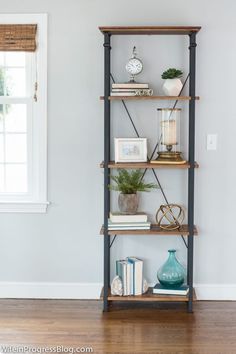 a book shelf with books and plants on it in the corner of a living room