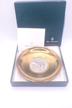 a gold plate in a black box with a white and blue label on the lid