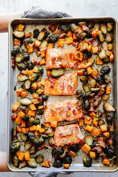 salmon and roasted vegetables on a baking sheet with someone holding the dish in their hands