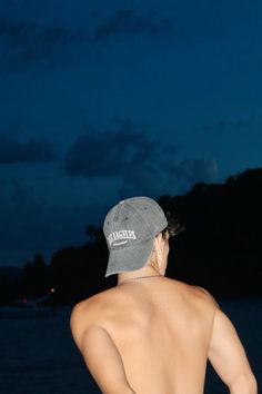 a shirtless man standing in front of the ocean at night with his back to the camera