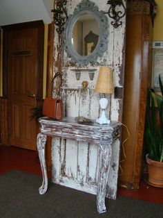 an old white table with a mirror and lamp on it in a living room area