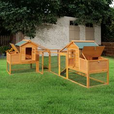 three wooden chicken coops sitting on top of green grass in front of a brick building