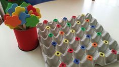 an egg carton with colorful magnets on it next to a red vase filled with flowers