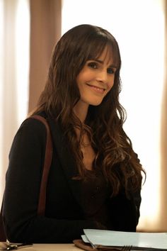 a woman sitting at a table with a book and pen in her hand, smiling