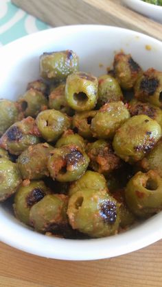 a white bowl filled with green olives on top of a wooden table