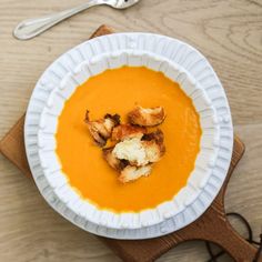 a white bowl filled with carrot soup on top of a wooden cutting board