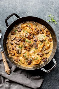 a skillet filled with chicken and mushrooms covered in gravy next to a spoon