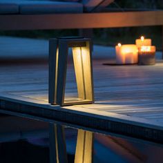 two lit candles sitting on top of a wooden floor next to a pool with water