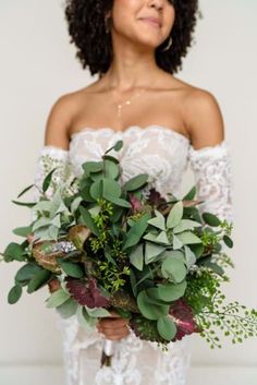 a woman holding a bouquet of flowers and greenery