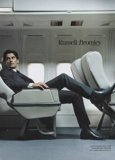 a man sitting in an airplane with his feet on the back of a chair while looking at the camera