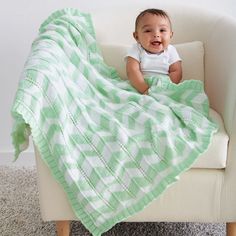 a baby sitting on a chair under a green and white blanket that is covering him