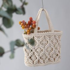 a white crocheted bag hanging from a tree branch with flowers in the front