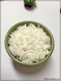 a green bowl filled with white rice next to peas and broccoli on a table