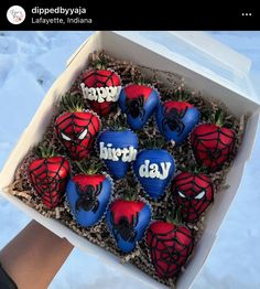 a box filled with cupcakes covered in frosting and decorated like spiderman faces