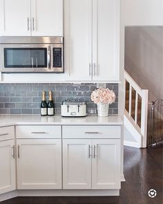 a kitchen with white cabinets and gray tile backsplashing, wine bottles on the counter