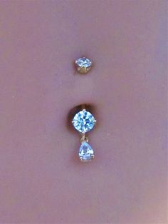 two diamond earrings sitting on top of each other in front of a pink background,