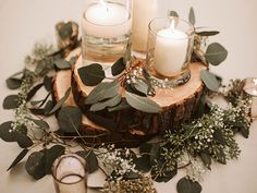 candles and greenery are arranged on a wood slice