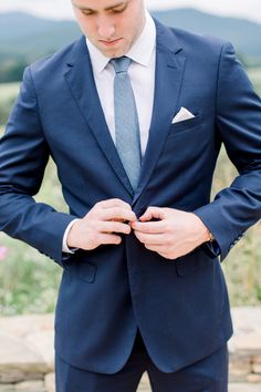 a man in a blue suit and tie is looking down at his pocket while standing outside