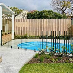 an empty swimming pool in front of a wooden fenced area with trees and bushes