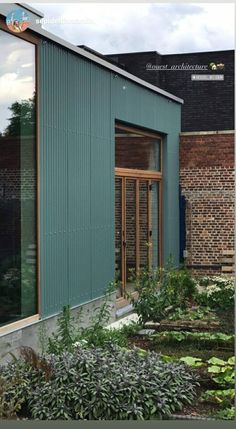 an image of a building that is made out of metal and wood with plants in the foreground