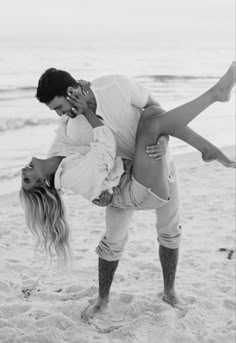 a man and woman kissing on the beach while holding each other's leg up