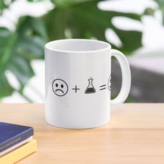 a white coffee mug sitting on top of a wooden table next to a book and plant