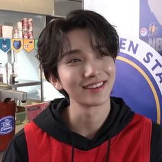 a young man standing in front of a sign and smiling at the camera while wearing a red hoodie