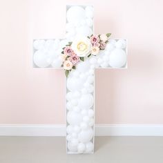 a cross made out of balloons with flowers on the front and back side, against a pink wall