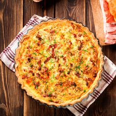 a quiche with bacon, cheese and green onions in a pie pan on a wooden table