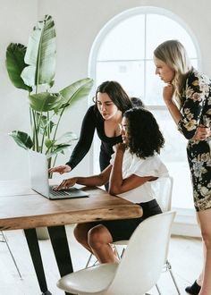 three women sitting at a table with a laptop