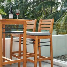 two wooden bar stools sitting next to a table with wine glasses on top of it