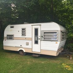 an old camper trailer is parked in the grass next to some trees and bushes