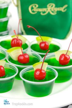 small cups filled with green jello and cherries on a white plate next to a green bag