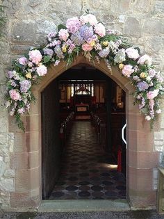 an archway decorated with flowers and greenery in front of a stone church entrance way