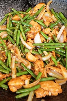 green beans, onions and chicken are being cooked in a wok on the stove